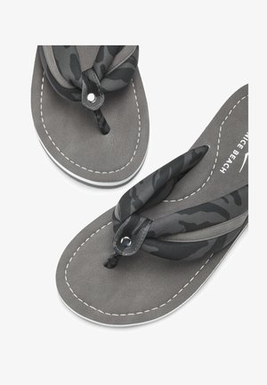 Paar grijze slippers met gevoerde zwarte camouflage stoffen bandjes en witte gestikte details op het voetbed en de zoolrand.