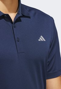 Mornarsko plava polo majica izrađena od glatkog materijala, sa šiljastim ovratnikom, zatvaranjem na gumbe i svijetlosivim logotipom na lijevoj strani prsnog dela.