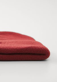 Rode gebreide beanie gevouwen aan de rand, die een gestructureerd patroon laat zien, een gladde afwerking en een zacht, dik materiaal.