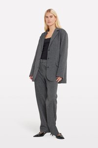 Un costume gris texturé comprenant un blazer ample avec des revers crantés et un pantalon large. Associé à un haut noir et des chaussures noires à bout pointu.
