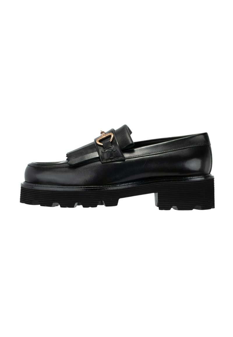 Mocasín de cuero negro con suela gruesa y estriada, detalle de flecos y hebilla en tono dorado sobre fondo blanco.