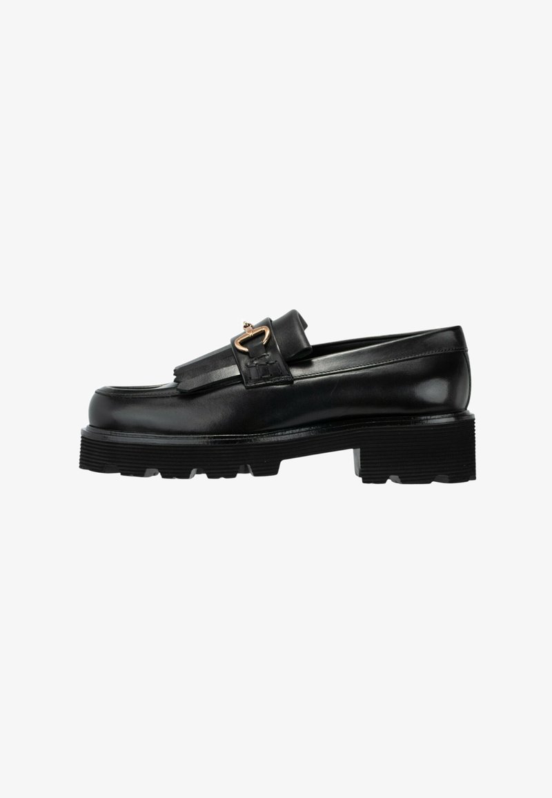 Zwarte leren loafers met dikke gegroefde zool, franjes en een gouden gesp op een witte achtergrond.