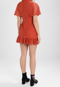 Red lace dress with short sleeves, flared hem, and a fitted bodice. Worn with black ankle boots featuring floral embroidery.