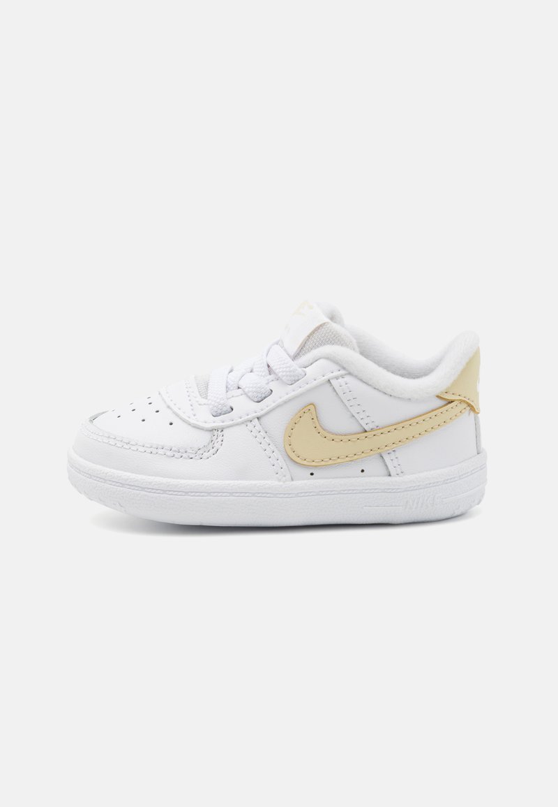Baskets en cuir blanc avec des accents beige, dotées d'un système de laçage, d'une boîte à orteils perforée et d'un emblématique swoosh beige de Nike sur le côté.