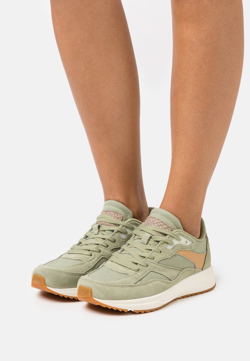 Jasnozielone buty sportowe wykonane z zamszowych i siateczkowych materiałów, z fakturowanymi sznurowadłami oraz podeszwą gumową. Posiadają brązowy akcent po boku.