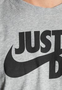 Pilkos medvilninės marškinėliai su dideliu juodu Nike logotipu ir tekstu "JUST DO IT" paryškintomis, didžiosiomis raidėmis. Trumpas, apvalus kaklas.