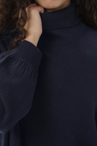 Marineblå genser med høy hals laget av mykt, strukturert stoff med ribbet detaljering ved kragen og ermene. Avslappet passform.