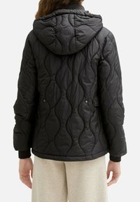 Doudoune matelassée noire avec capuche. Caractérisée par un motif de piqûres ondulées et des poignets côtelés. Texture lisse et matière légère.