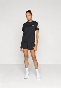 Camiseta deportiva negra y pantalones cortos, ambos con rayas y logotipos blancos. Material parece ligero; textura suave.