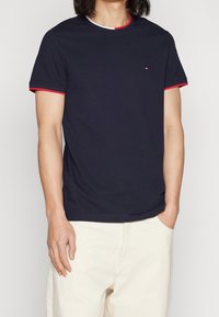 T-shirt in cotone blu navy con colletto e bande sulle maniche in contrasto rosso e bianco. Maniche corte, scollo tondo, design aderente.