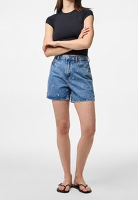 Shorts de mezclilla con bordado floral, de tiro alto y con el dobladillo deshilachado. Combinados con una camiseta negra ajustada y chanclas negras.