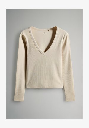 Top beige a maniche lunghe con scollatura a V. Presenta un tessuto a coste testurizzato e un design cropped. Stile semplice e minimalista.