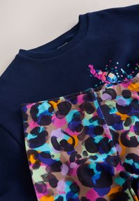 Navy sweatshirt with sequined design, paired with colorful patterned leggings featuring abstract shapes in purple, blue, and pink tones.