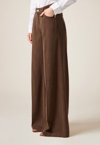 Pantalones marrones de pierna ancha hechos de tejido texturizado, con bolsillos laterales, botones en tono dorado y un diseño de cintura alta.