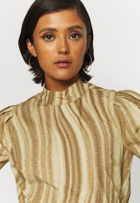 Blusa de gola alta riscada em castanho e bege, com mangas bufantes, fabricada em tecido suave, apresentando um leve brilho e textura.