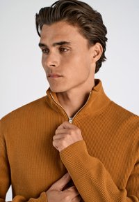 Maglione a coste con zip di colore arancio bruciato, caratterizzato da un alto colletto e polsini aderenti. Il tessuto appare morbido con una superficie testurizzata.