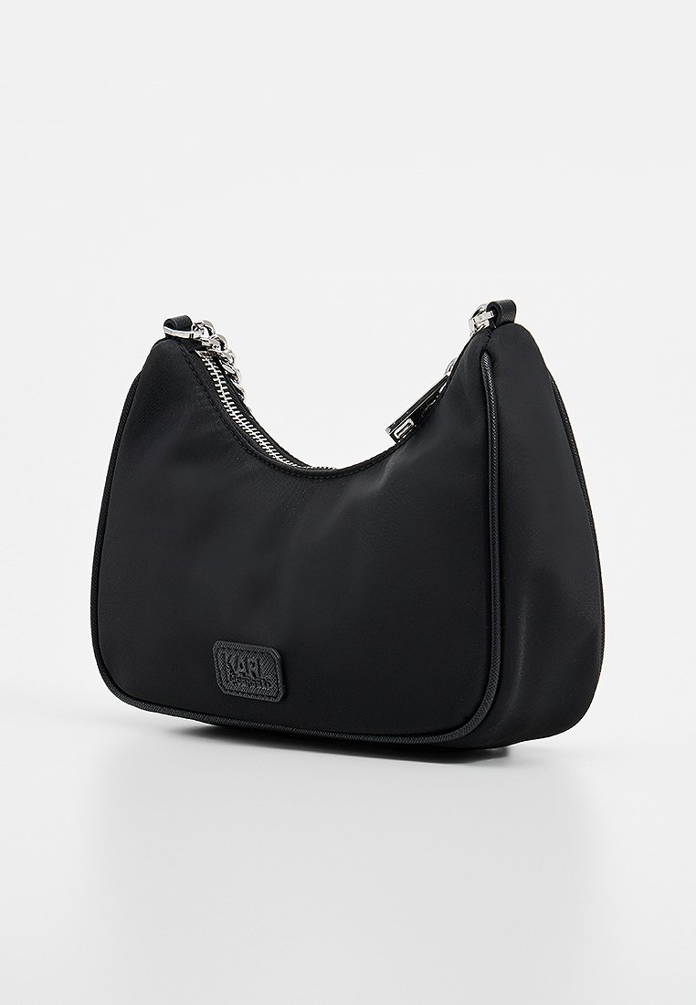 Petite sac à bandoulière noir avec chaîne en argent et fermeture éclair, présentant un patch de marque discret à l'avant.
