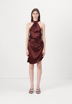 Satin halterneck-klänning i vinröd, asymmetrisk fåll, slät yta, figursydd siluett, kombinerad med svarta sandaler med remmar.