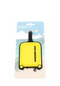 Étiquette de bagage en forme de valise jaune avec des bords noirs et le texte "MANDARINA DUCK", attachée à un emballage bleu et blanc sur le thème du voyage.