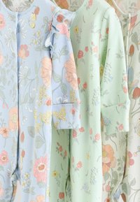 Body de bébé floraux en bleu pastel, vert et crème ; matériaux en coton doux avec différents motifs de fleurs et détails de manches volantes.