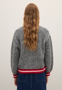 Jersey de punto con patrón de espiga en negro, blanco y rojo; cuenta con cuello redondo y borde acanalado. Vista trasera muestra tejido texturizado.