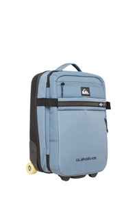 Wheeled backpack in light blue fabric with black accents, featuring a front zip pocket, reinforced handles, and durable rubber wheels.