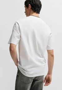 Hvid t-shirt med korte ærmer, afslappet pasform, rund halsudskæring og glat tekstur, parret med mørke jeans. Enkel og minimalistisk design.