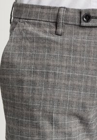 Šedé kostkované kalhoty s texturovanou tkaničkou, plochým předním dílem a jedním knoflíkem na zapínání v pase. Mezi detaily patří jemné vzory kostek.