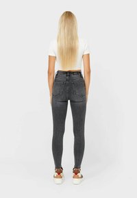 Jeans skinny grigi a vita alta, con tasche posteriori e una leggera sfumatura, abbinati a sneakers bianche e a un top bianco corto.