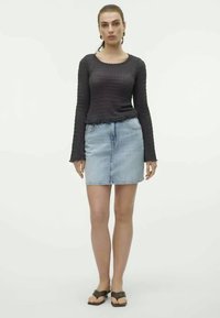 Top preto de manga longa texturizado, combinado com uma mini saia de ganga azul clara. Modelo usa sandálias escuras. Design simples e minimalista.
