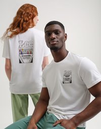 Due modelli indossano t-shirt bianche con stampe di scatole di pastelli Crayola neri; uno mostra il retro, l'altro il davanti, entrambi abbinati a pantaloni a righe verdi.