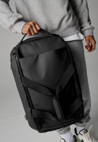 Zaino nero realizzato in materiale resistente, con design minimalista, spallacci regolabili e una tasca frontale con zip nascosta.