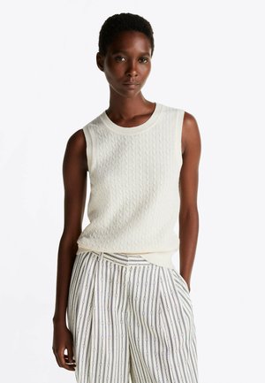 Ärmelloses Creme-Stricktop mit Zopfmuster, rundem Halsausschnitt und lockerer Passform; kombiniert mit gestreiften, hoch taillierten Hosen.