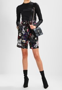 Black long-sleeve top, floral-patterned shorts with a tied waist, and black ankle boots, complemented by a small black handbag.