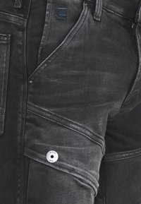 Svarta denim cargobyxor med synlig kontrastsöm, vinklade fickor och en framträdande denimknapp med "G-Star RAW"-logotyp.