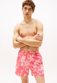 Bañador corto floral rosa con cintura ajustable, que presenta una textura de tela brillante y un logo bordado en el costado.