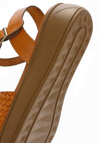 Sandalo platform marrone con cinturini in pelle intrecciata e suola in gomma strutturata. Il tacco presenta un motivo a scanalature diagonali per una migliore aderenza.