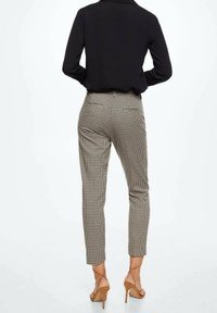 Pantalons à carreaux en noir et blanc, coupe slim avec poches arrière, associés à des talons strappy beige et un blouse noire.