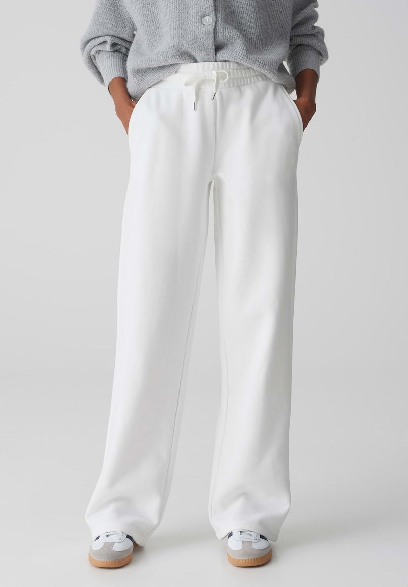 Weiße, weite Sweatpants mit einem elastischen Bund, Kordelzugdetail, Seitentaschen und einer glatten, weichen Stoffstruktur.