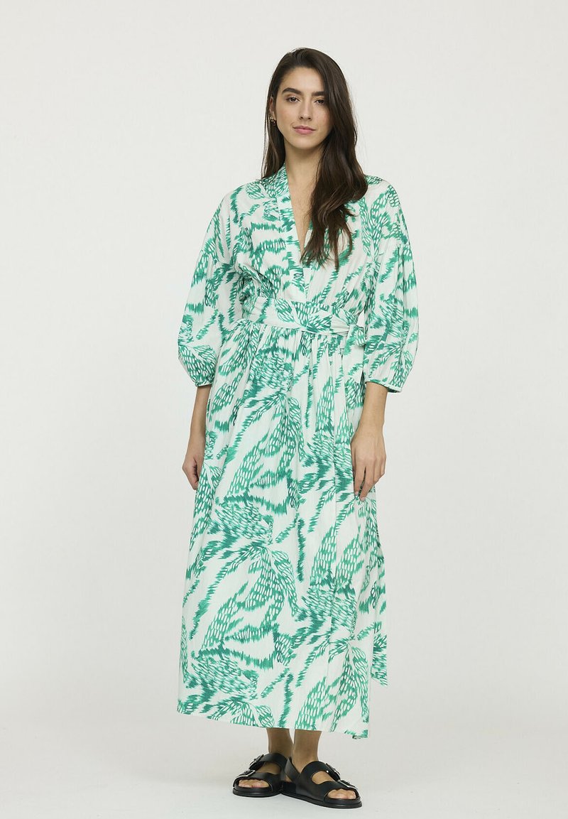 Robe enveloppante verte et blanche à motifs avec des manches longues et une ceinture à la taille, fabriquée dans un tissu léger, présentant un design fluide.