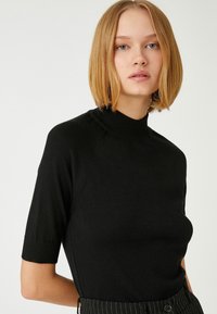 Sort kortærmet top med en høj hals-design, lavet af glat stof. Har raglanærmer og en tætsiddende silhuet. Ingen synlige mønstre.