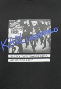 T-shirt nera con una grafica grigia di una folla, inclusa la scritta "KARL LAGERFELD" in blu e una citazione in bianco nella parte inferiore.