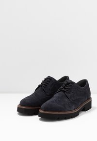 Dunkelblaue Wildleder-Broschürenschuhe mit Broguemuster, Schnürdesign, dickem schwarzen Gummisohle und braunem Kontraststich entlang der Kante.