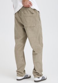 Beige corduroy pants with a relaxed fit, featuring a back pocket and elastic waistband. Worn with white sneakers displaying black stripes.