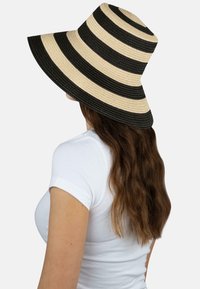 Breiter Strohhut mit abwechselnden schwarzen und beigen Streifen, der eine strukturierte Oberfläche und eine flexible Form zum Sonnenschutz hat.