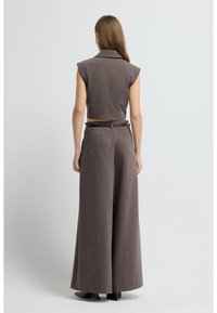 Hnědý bezrukávový krátký top s límcem, kombinovaný s kalhotami s vysokým pasem a širokými nohavicemi. Látka vypadá texturovaně s elegantním střihem.