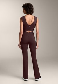 Sutien sport scurt, maro, cu un decolteu în V adânc la spate, asortat cu pantaloni evazați, cu talie înaltă, în aceeași nuanță. Material neted cu cusături minime, siluetă ajustată.