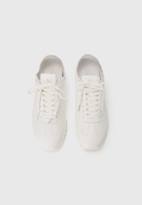 Weiße Sneaker aus glattem Leder, mit runder Zehenpartie, tonalem Nähen, flachen Schnürsenkeln und gepolsterten Sohlen. Minimalistisches Design mit dezentem Branding.