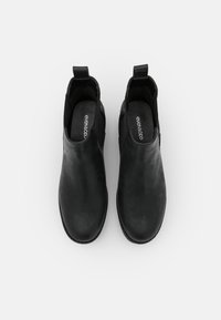 Botas de tobillo negras con un acabado de cuero liso, paneles laterales elásticos y una lengüeta en el talón. Forro interno y plantilla visibles.