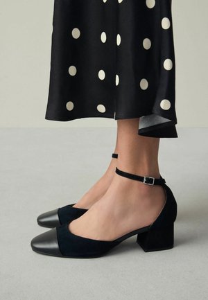 Chaussures à talons carrés en daim noir avec un bout en cuir noir contrastant et une bride à la cheville ornée d'une petite boucle.